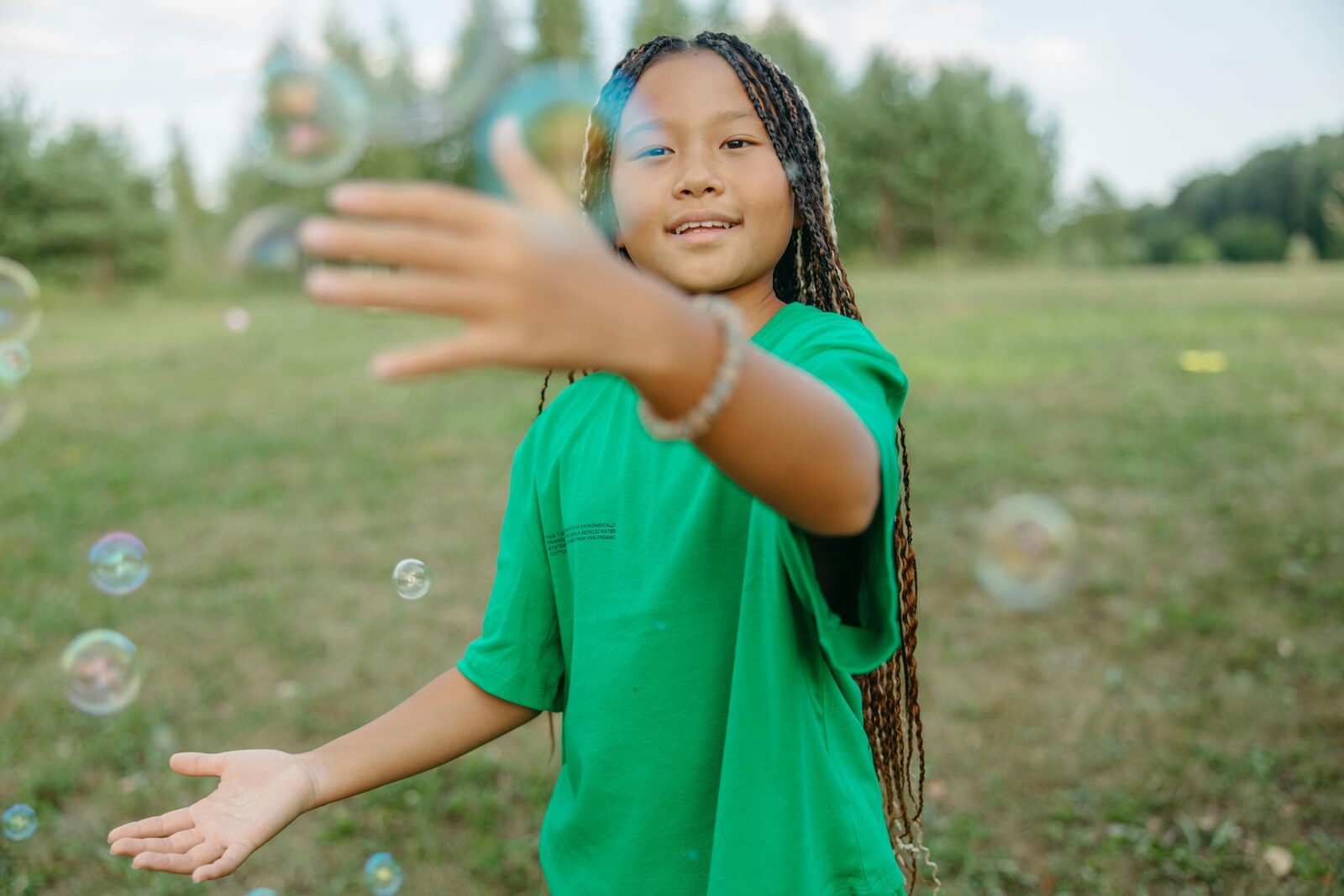 Girl aged around ten smiling and reaching for soap bubbles in a field