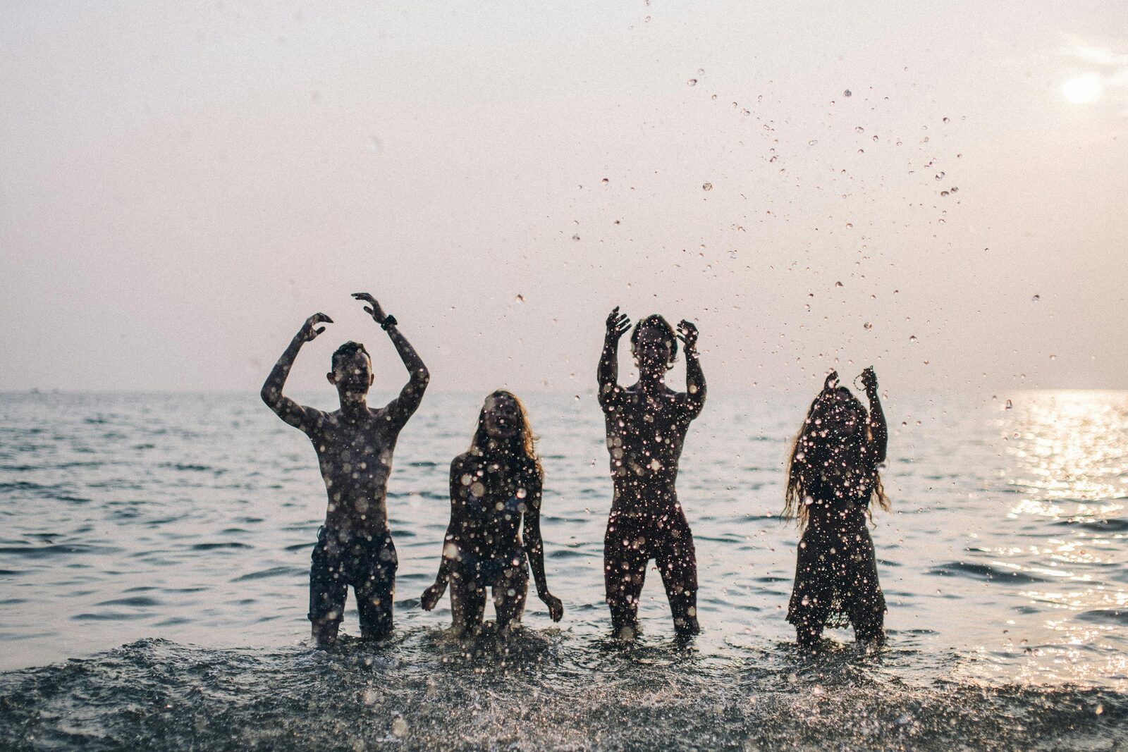 Silhouettes of four teenagers splashing in the sea at sunset